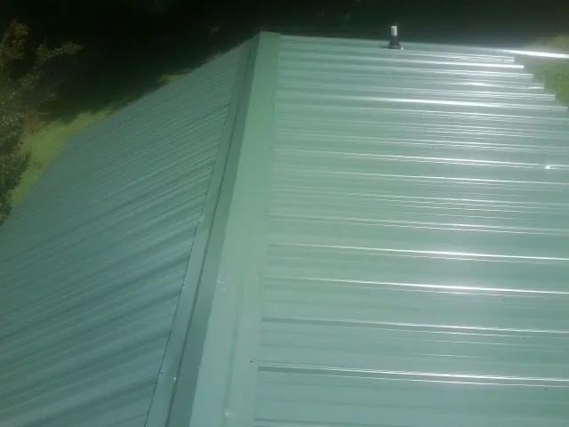 New green metal panels meeting at the ridge of a roof — Flat Roof Repair work by our crew in Dayton
